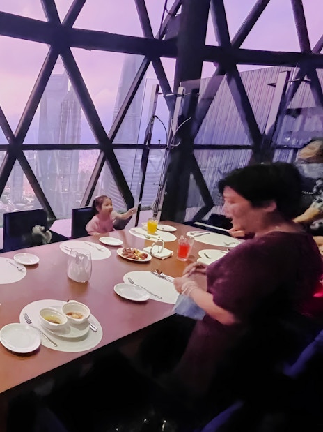 Family dining at revolving restaurant, Oriental Pearl Tower, Shanghai, with city skyline view.