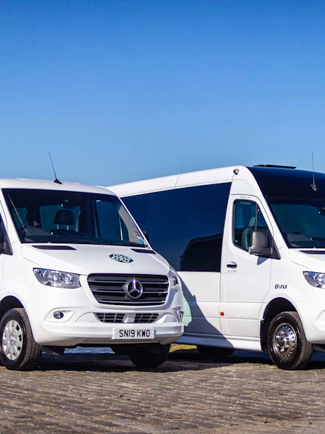 Private air-conditioned transfer vans parked by a waterfront.