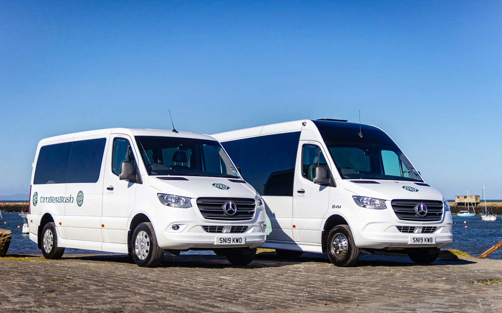 Private air-conditioned transfer vans parked by a waterfront.