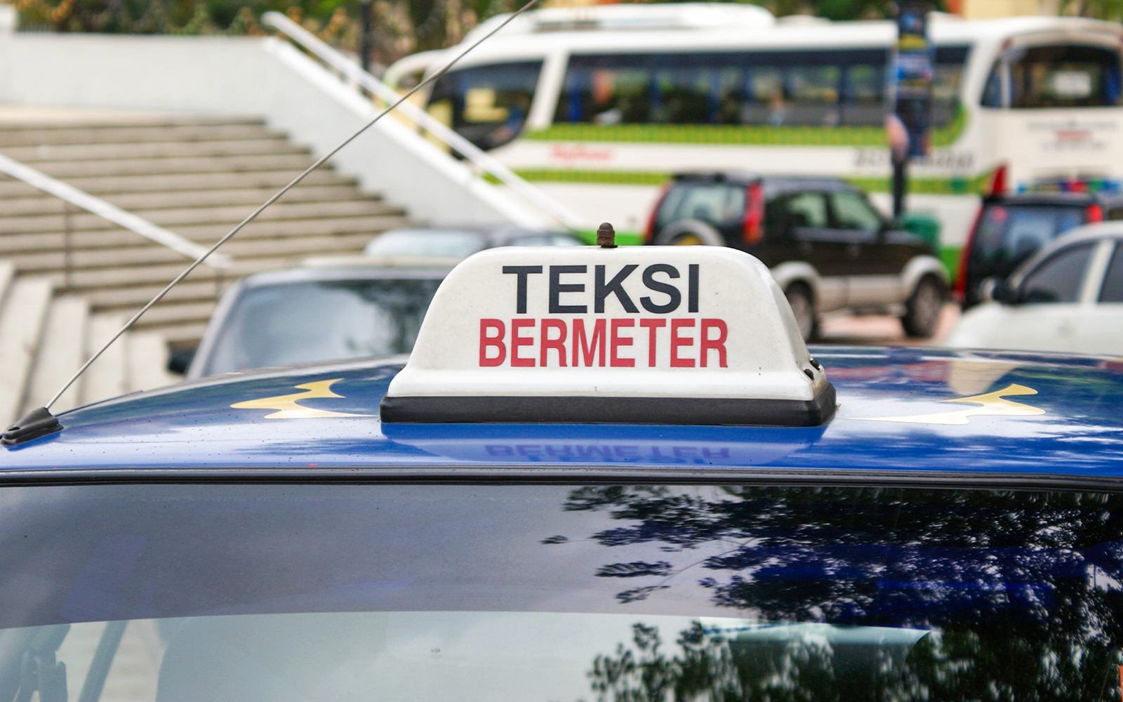 Yellow taxi in Kuala Lumpur, Malaysia, with city skyline in the background.