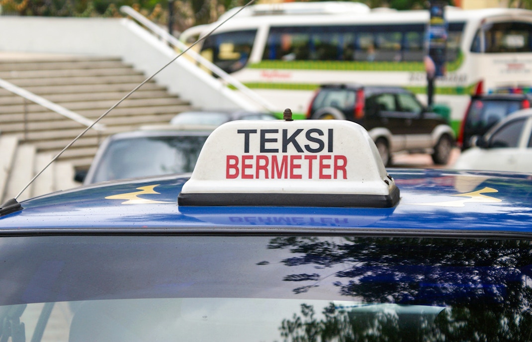 Yellow taxi in Kuala Lumpur, Malaysia, with city skyline in the background.