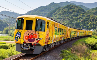 Colorful train with cartoon characters on JR PASS Kagawa Mini Rail, surrounded by lush green hills.