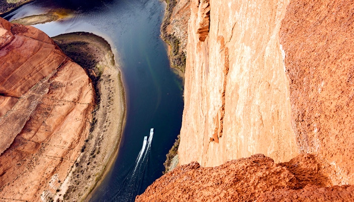 Two boats navigating the Colorado River at Horseshoe Bend, deep canyon view.