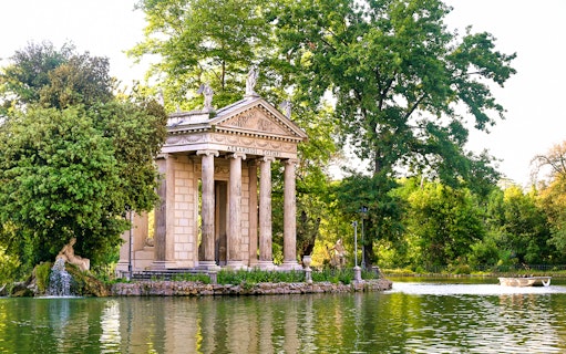 Temple of Asclepius in Villa Borghese, Rome, surrounded by trees and a lake.