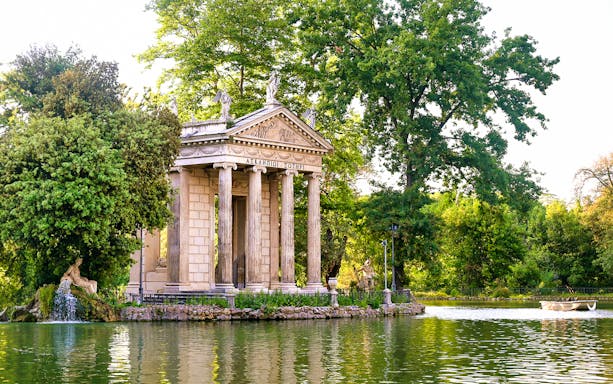 Temple of Asclepius in Villa Borghese, Rome, surrounded by trees and a lake.