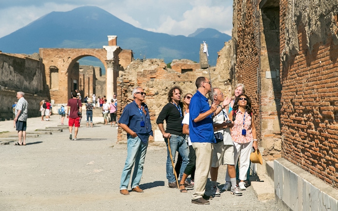 Guide explaining Pompeii ruins to tourists with Mount Vesuvius in the background.