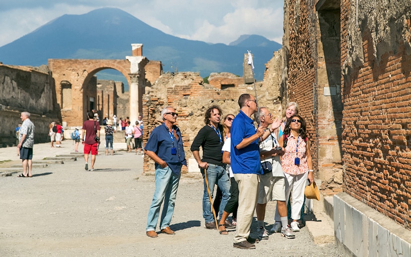 Guide explaining Pompeii ruins to tourists with Mount Vesuvius in the background.