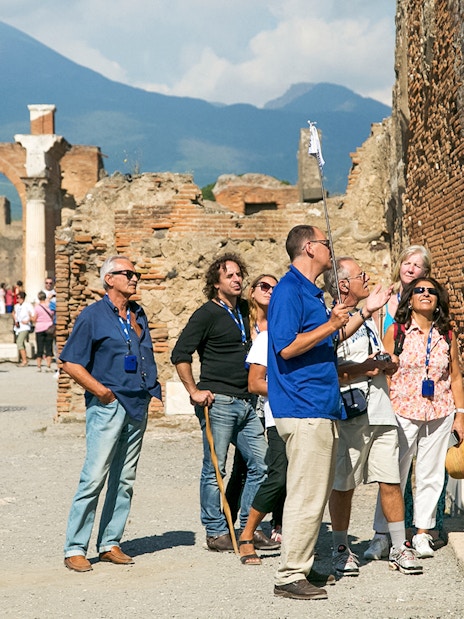 Guide explaining Pompeii ruins to tourists with Mount Vesuvius in the background.