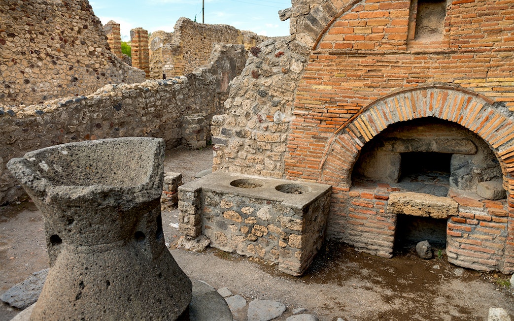Ancient ruins of a bakery in Pompeii with stone oven and millstone.