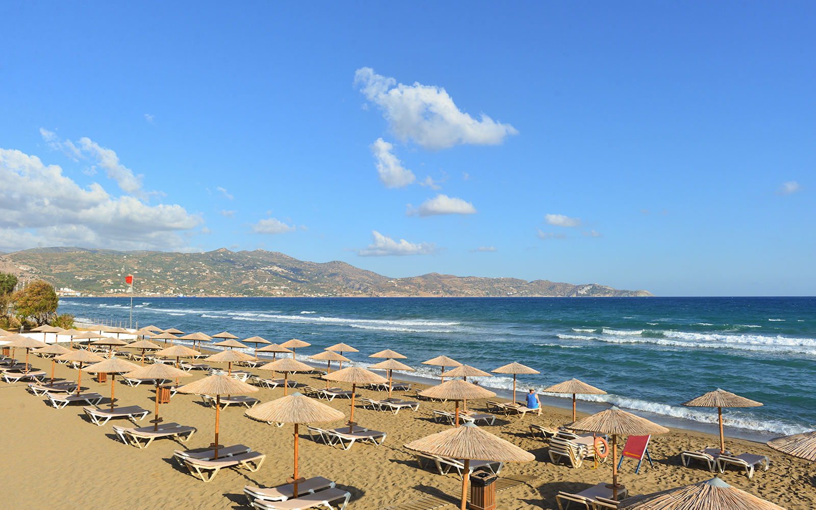 Beach with sun loungers and umbrellas in Heraklion, Crete, with mountains in the background.
