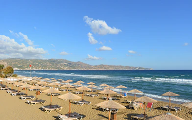 Beach with sun loungers and umbrellas in Heraklion, Crete, with mountains in the background.