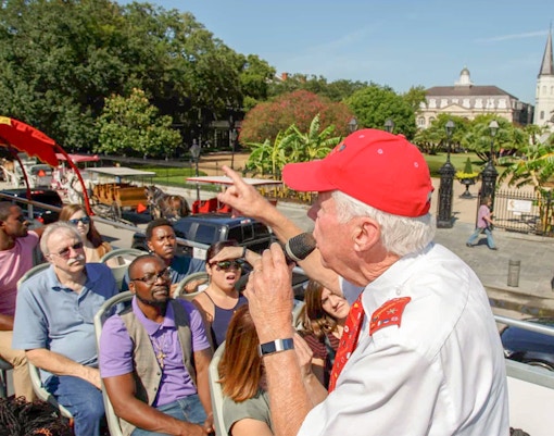 Double-decker bus on New Orleans Hop-On Hop-Off tour passing historic French Quarter buildings.
