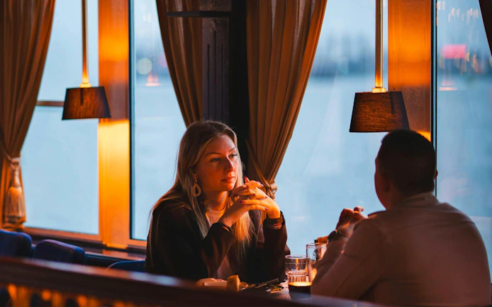 Couple dining on a pizza cruise with scenic window view.