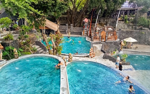 Kintamani hot springs with visitors enjoying multiple pools surrounded by lush greenery.