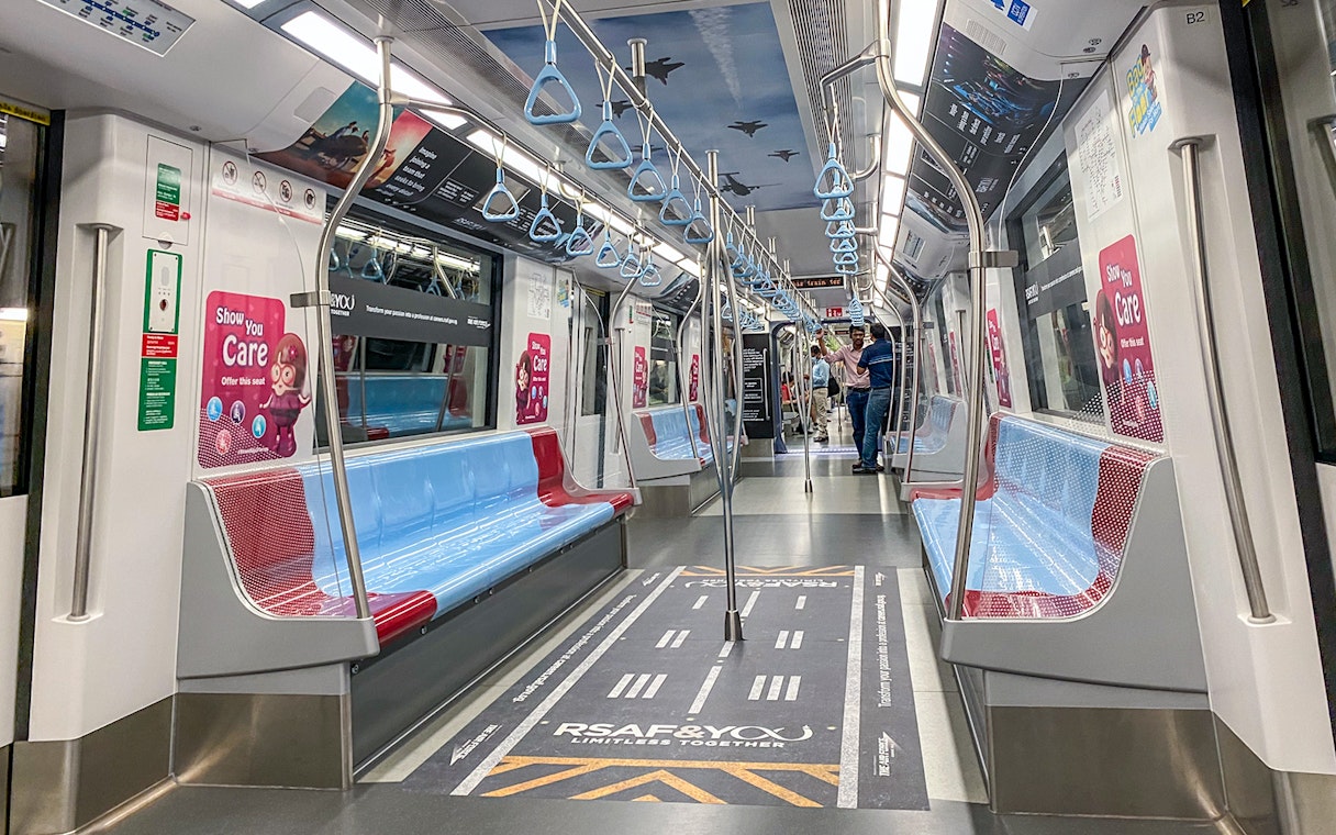 MRT train interior in Singapore with blue and red seats, overhead handles, and safety signage.