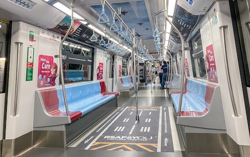 MRT train interior in Singapore with blue and red seats, overhead handles, and safety signage.