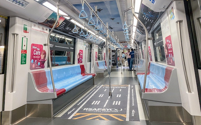 MRT train interior in Singapore with blue and red seats, overhead handles, and safety signage.