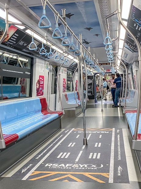 MRT train interior in Singapore with blue and red seats, overhead handles, and safety signage.