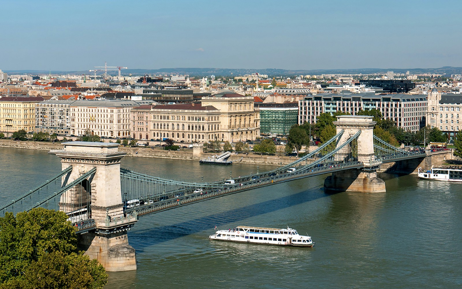 Budapest Danube River cruise boat passing under Chain Bridge with cityscape in the background.