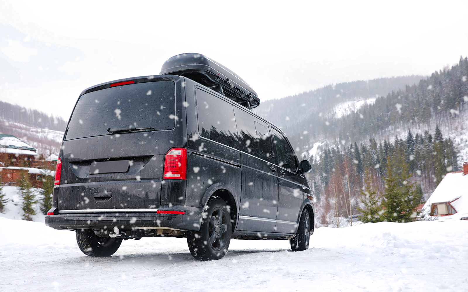 Black van driving on a snowy mountain road in winter.