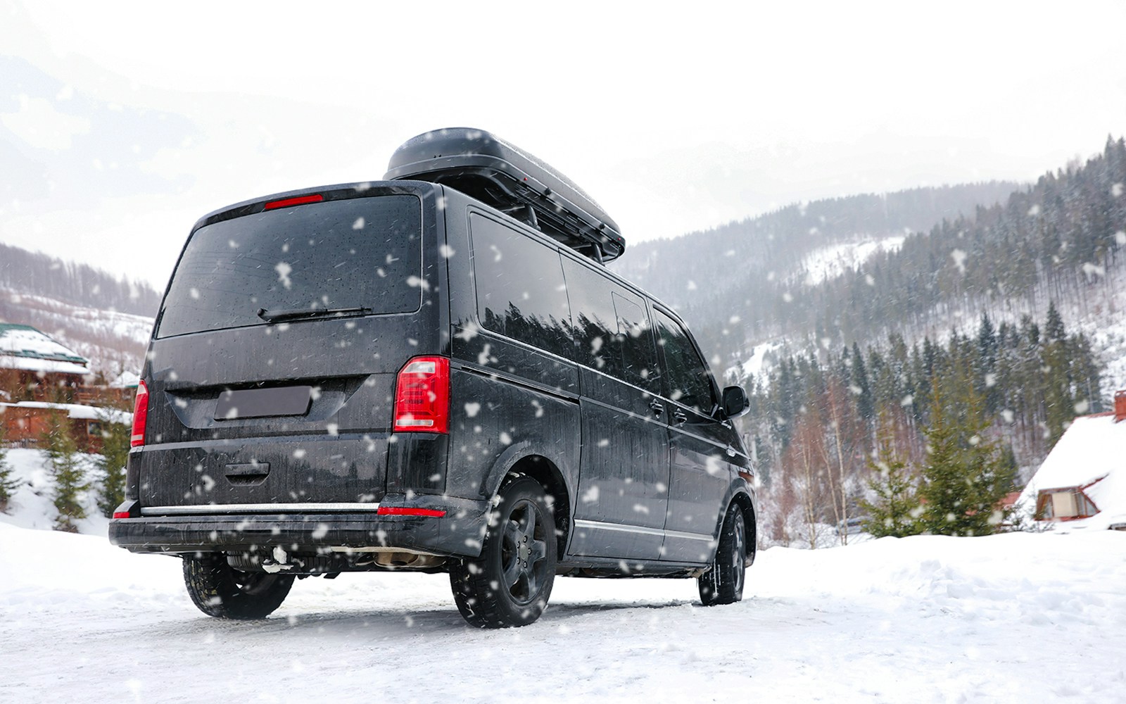 Black van driving on a snowy mountain road in winter.
