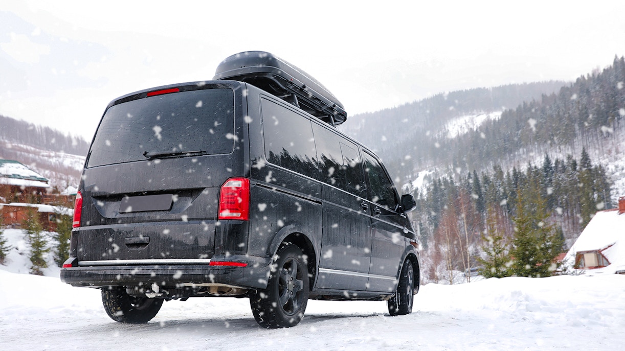 Black van driving on a snowy mountain road in winter.