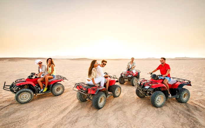 Group riding quad bikes at sunset in the Palmeraie desert.