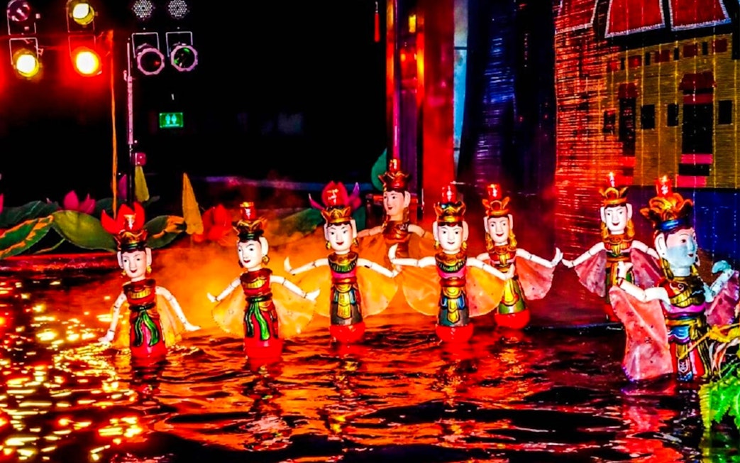 Female puppets in traditional attire perform at Thang Long Water Puppet Show, Hanoi, under red lights.