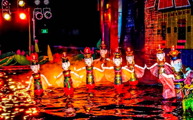Female puppets in traditional attire perform at Thang Long Water Puppet Show, Hanoi, under red lights.