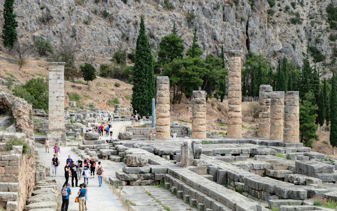Tourists exploring the ancient ruins of the Temple of Apollo in Delphi, Greece.