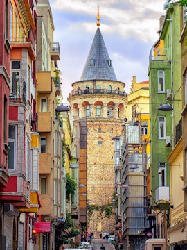 Galata Tower in Istanbul framed by colorful buildings on a narrow street.