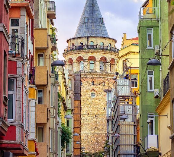 Galata Tower in Istanbul framed by colorful buildings on a narrow street.