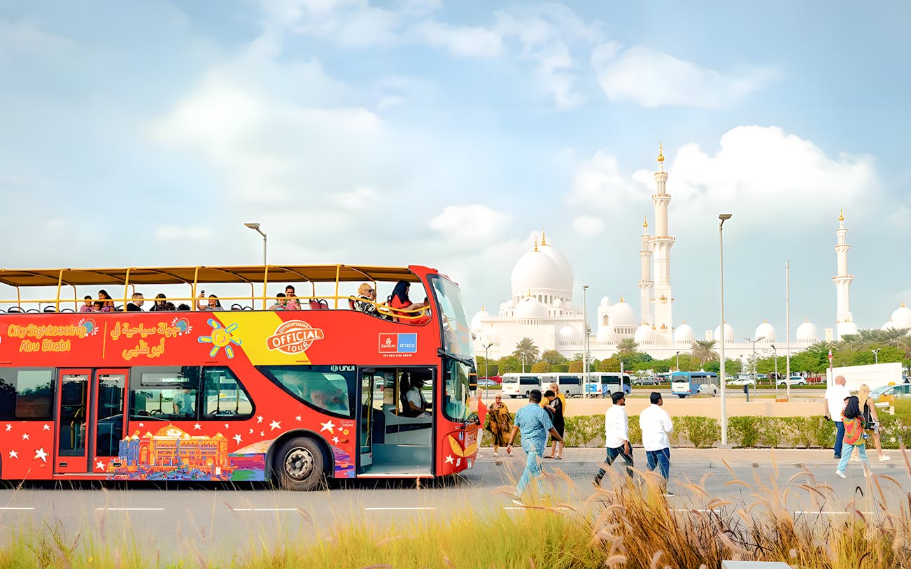 Open-top bus on Abu Dhabi city tour with Sheikh Zayed Grand Mosque in background.