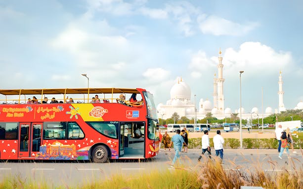 Open-top bus on Abu Dhabi city tour with Sheikh Zayed Grand Mosque in background.