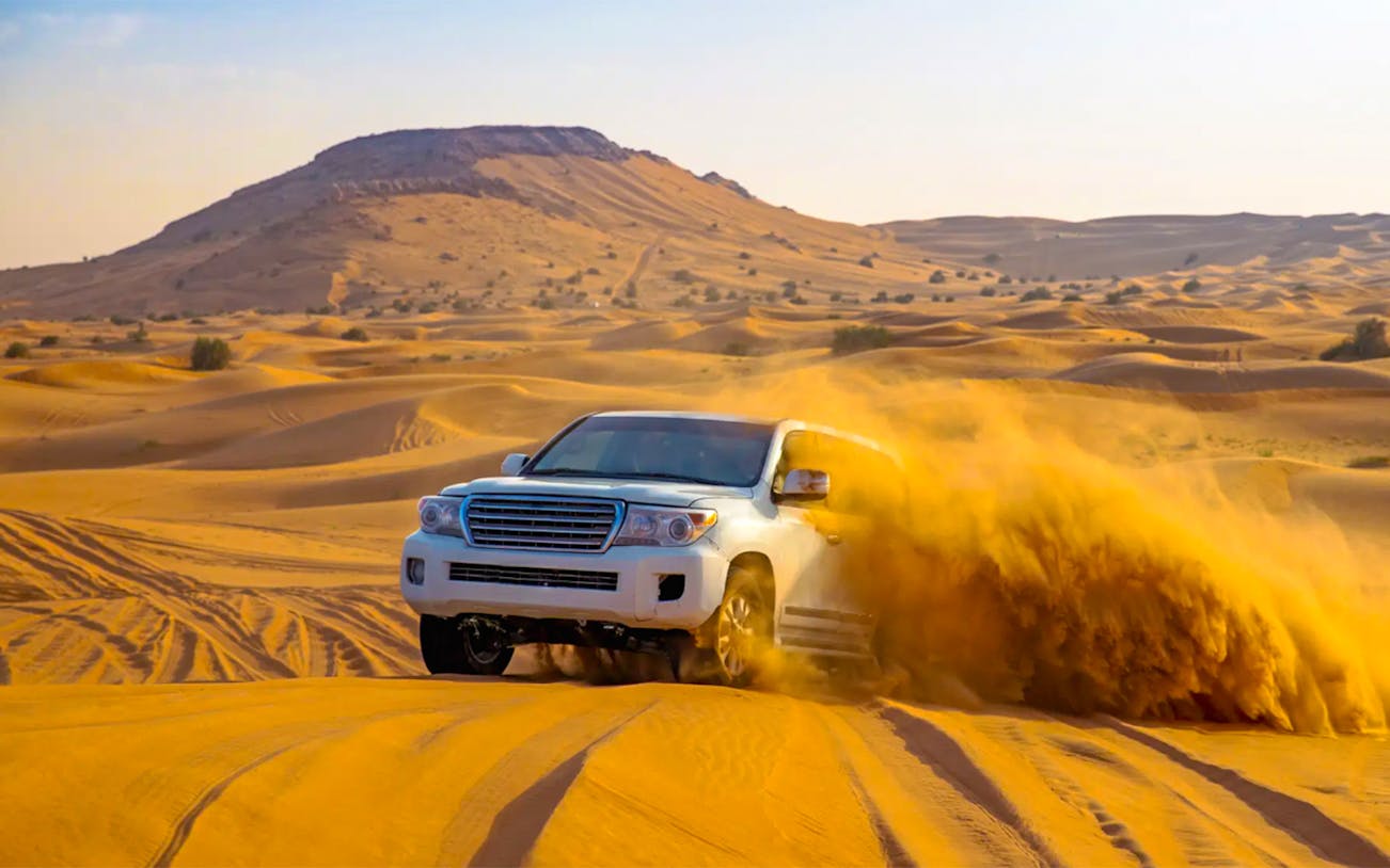 SUV driving through desert dunes during evening safari in Dubai.