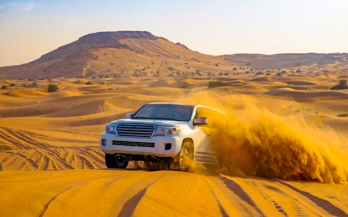 SUV driving through desert dunes during evening safari in Dubai.