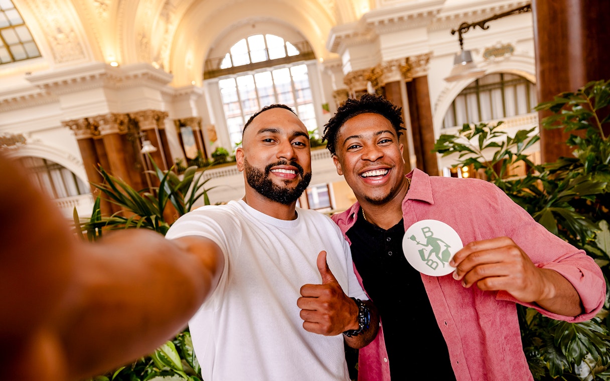 Guests enjoying Belgian Beer World Experience in Brussels, smiling with a beer coaster.