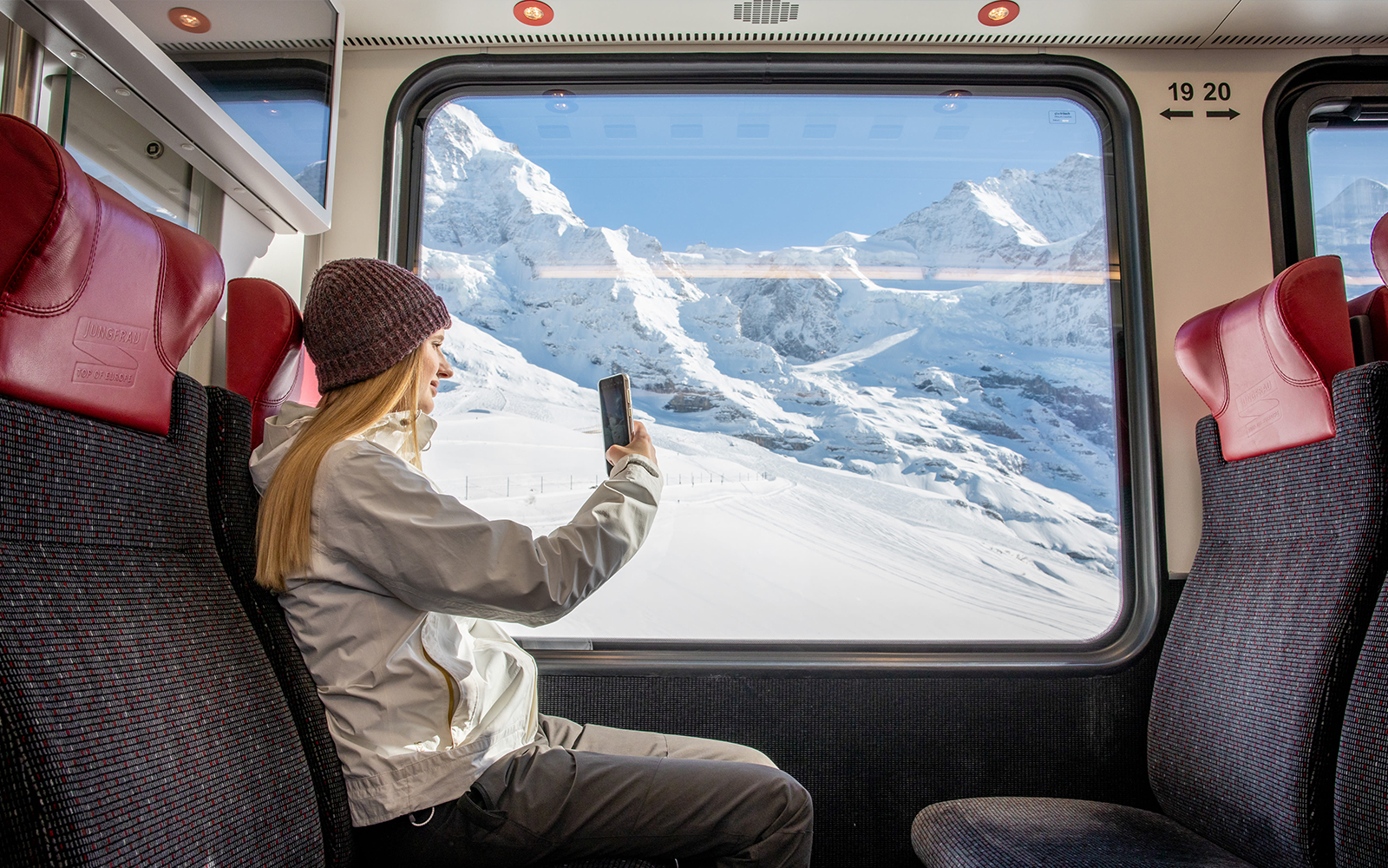 Traveller taking photo from Jungfraubahn train window with snowy Alps view.
