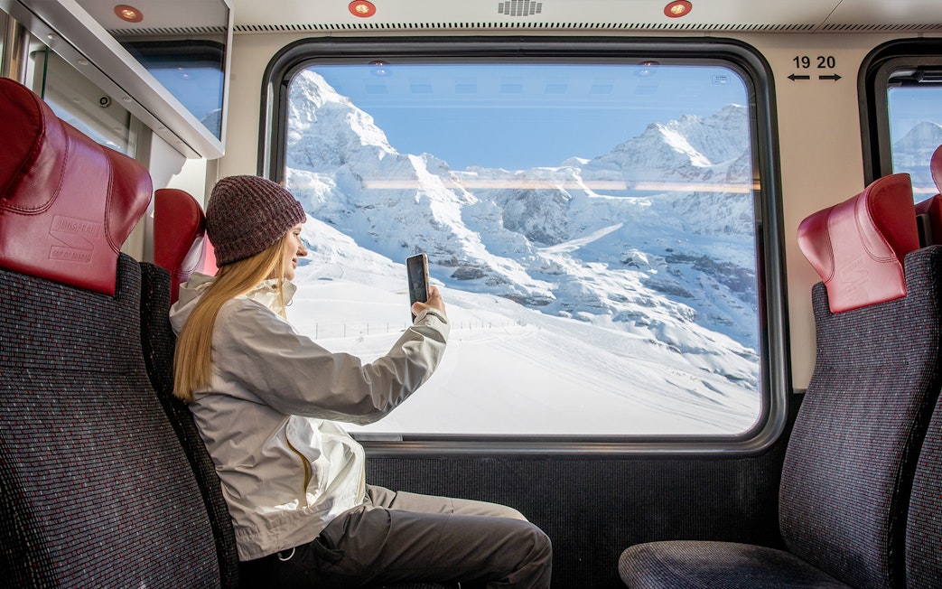 Traveller taking photo from Jungfraubahn train window with snowy Alps view.