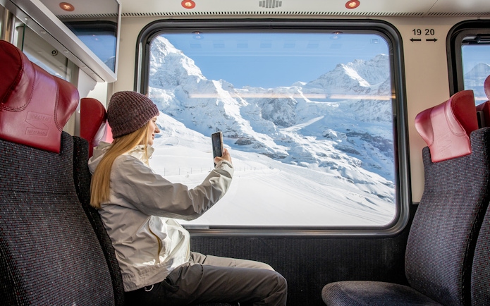 Traveller taking photo from Jungfraubahn train window with snowy Alps view.