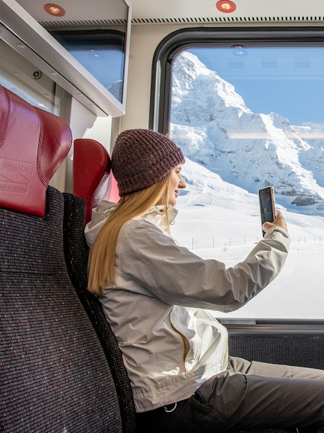 Traveller taking photo from Jungfraubahn train window with snowy Alps view.