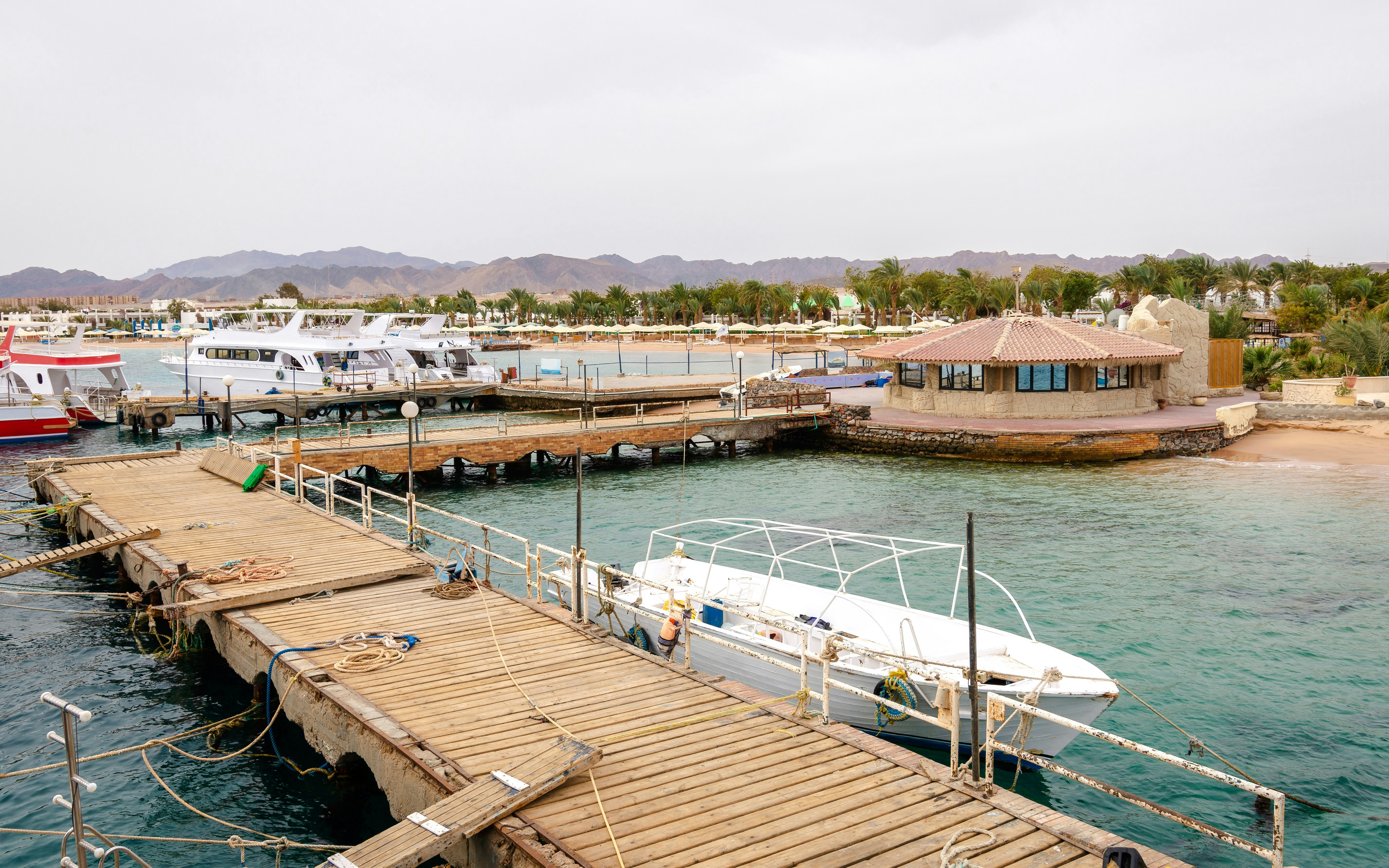 Safaga pier with boats and a coastal building on a cloudy day, Hurghada, Egypt.