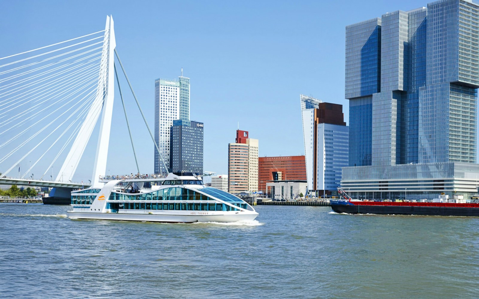 Cruise boat on Rotterdam's river with Erasmus Bridge and modern skyline.