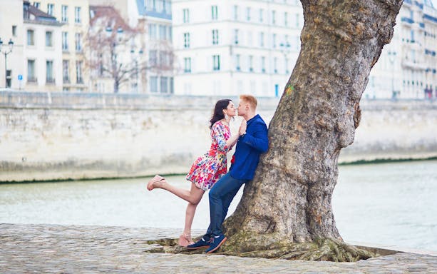 Couple kissing by a tree along the Seine River in Paris.