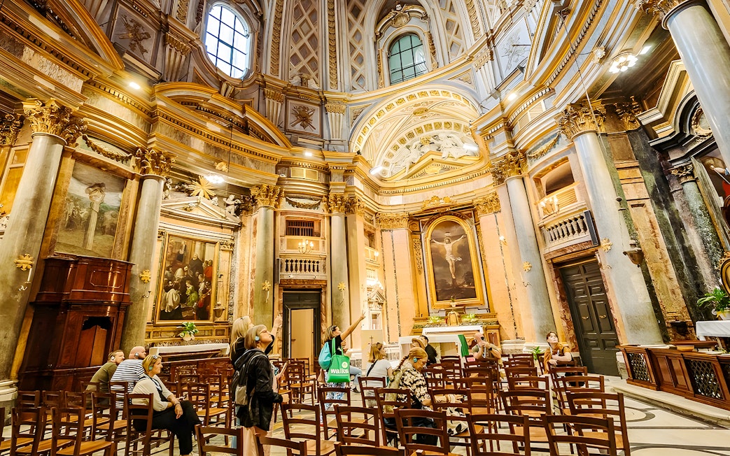 Interior of Basilica of San Nicola with visitors on a guided tour, featuring ornate architecture and religious artwork.
