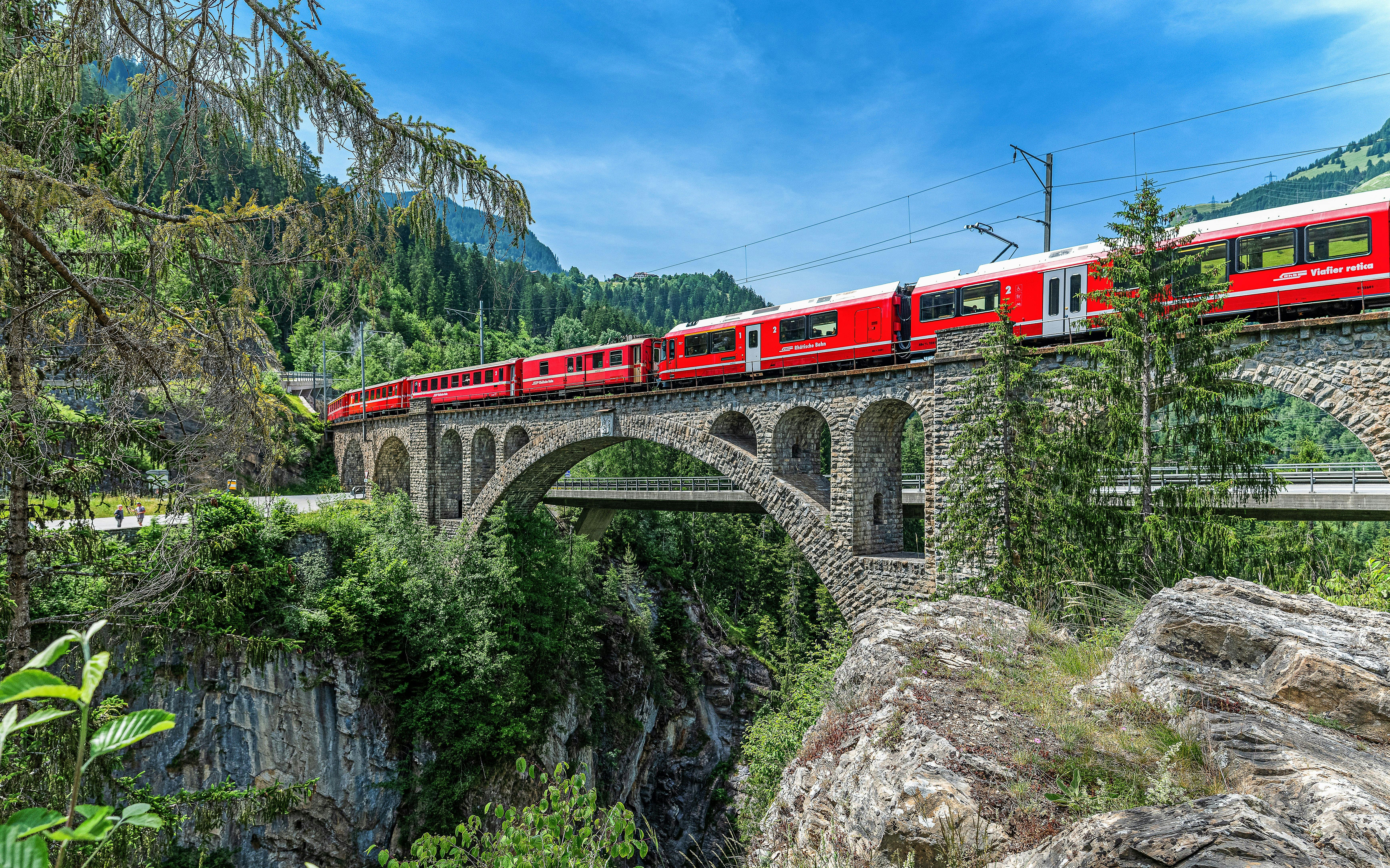 Bernina train crossing Solis Viaduct in Swiss Alps with lush greenery and rocky landscape.