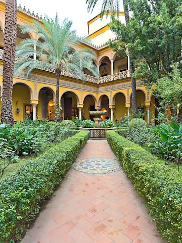 Courtyard of Palacio de las Dueñas in Seville with arches and lush greenery.