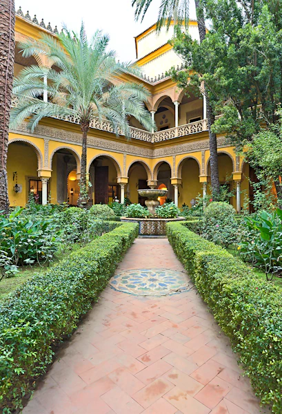 Courtyard of Palacio de las Dueñas in Seville with arches and lush greenery.