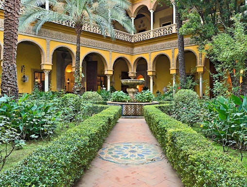 Courtyard of Palacio de las Dueñas in Seville with arches and lush greenery.