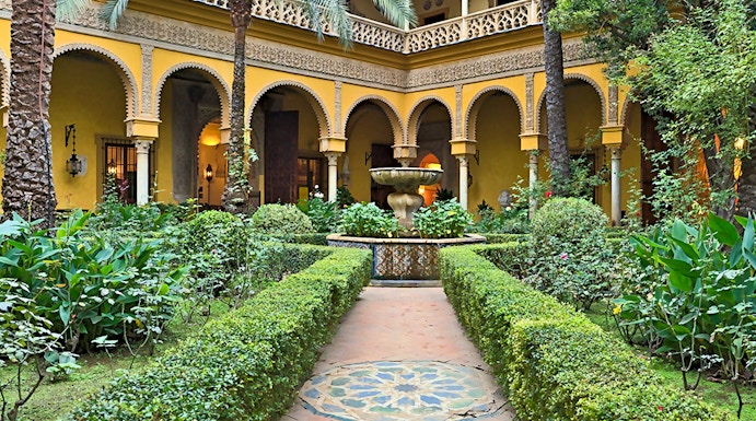 Courtyard of Palacio de las Dueñas in Seville with arches and lush greenery.